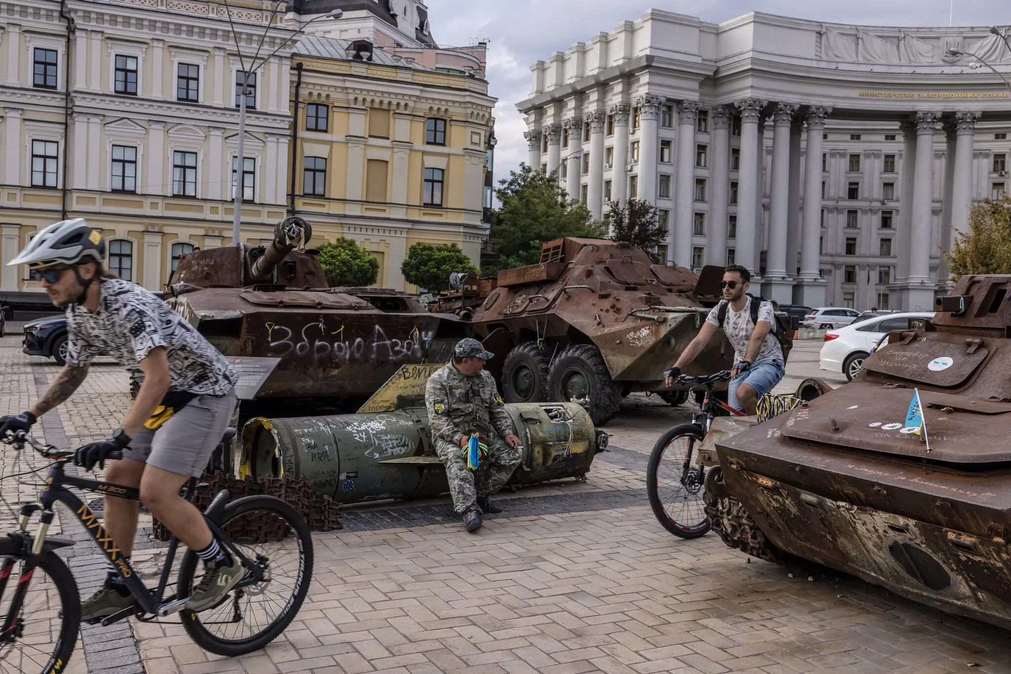 Чоловіки катаються на велосипедах виставкою знищеної військової техніки в Києві.